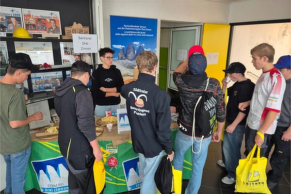 Our stand at the business day at the vocational training centre in Brunico: pupils at the table with cheese cubes in front of the Drei Zinnen Dairy roll-up